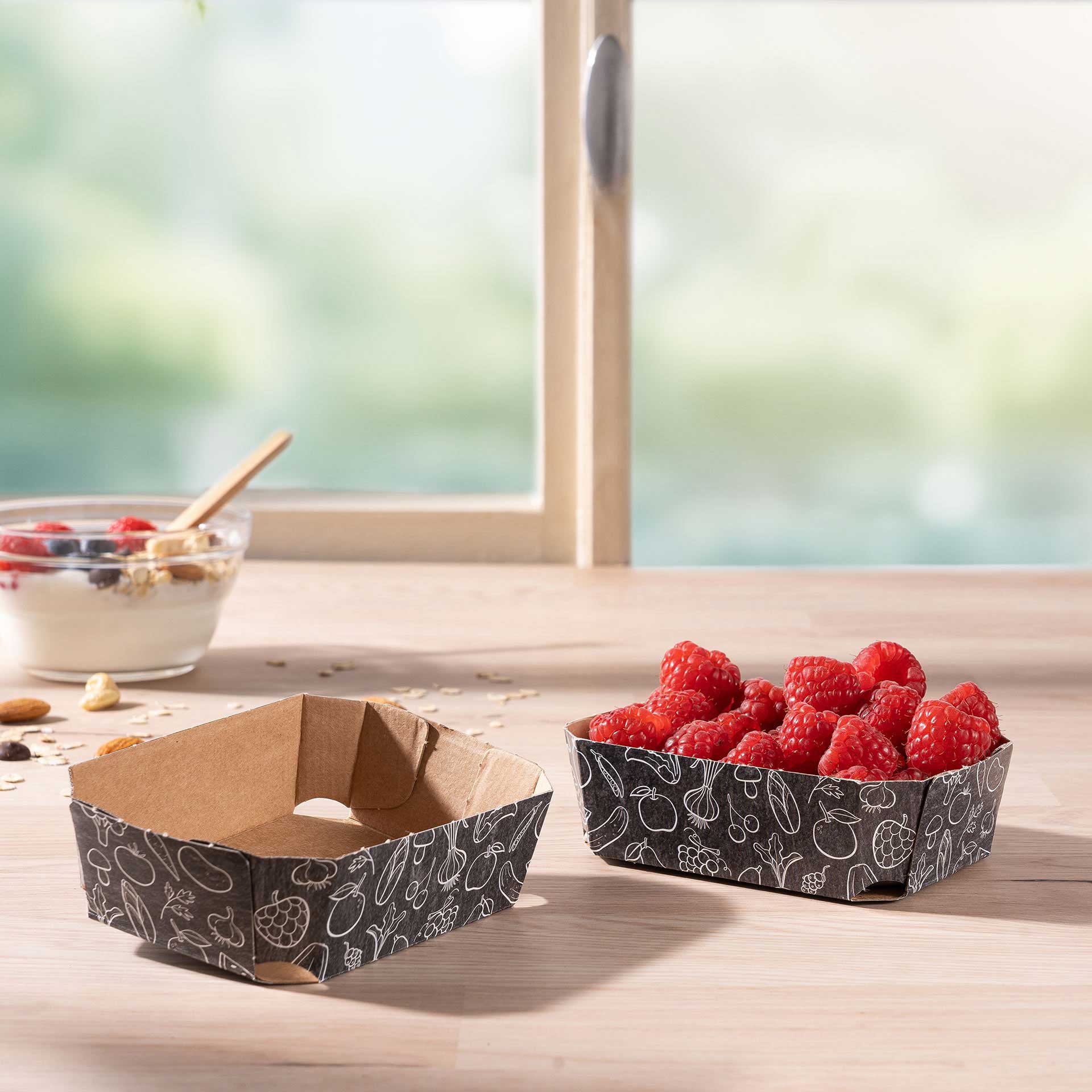 Zwei Beerenschalen aus Wellpappe 125g mit Himbeeren auf einem Tisch