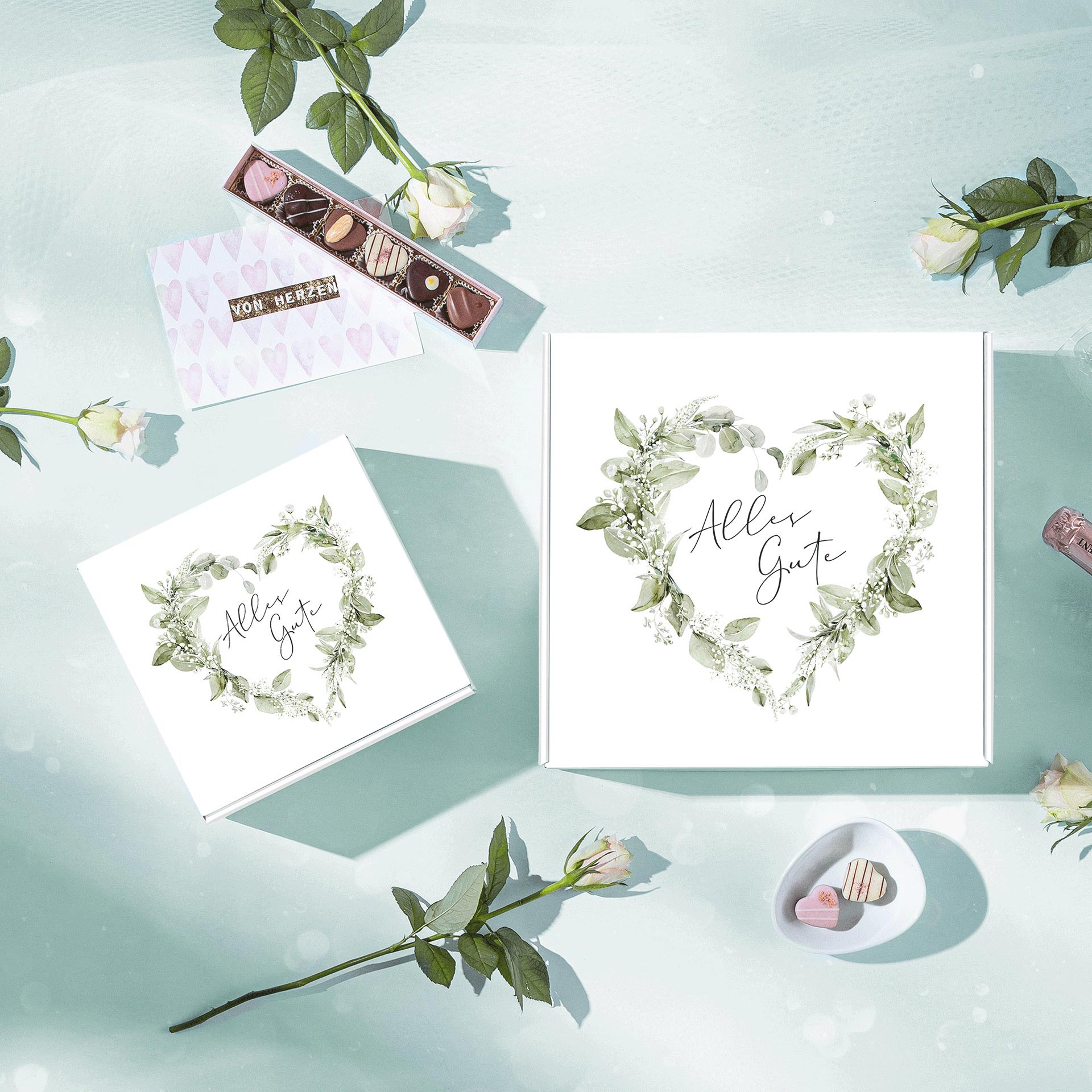 Weiße Geschenkboxen mit grünem Blattkranz und "Alles Gute"-Schriftzug im Quadrat