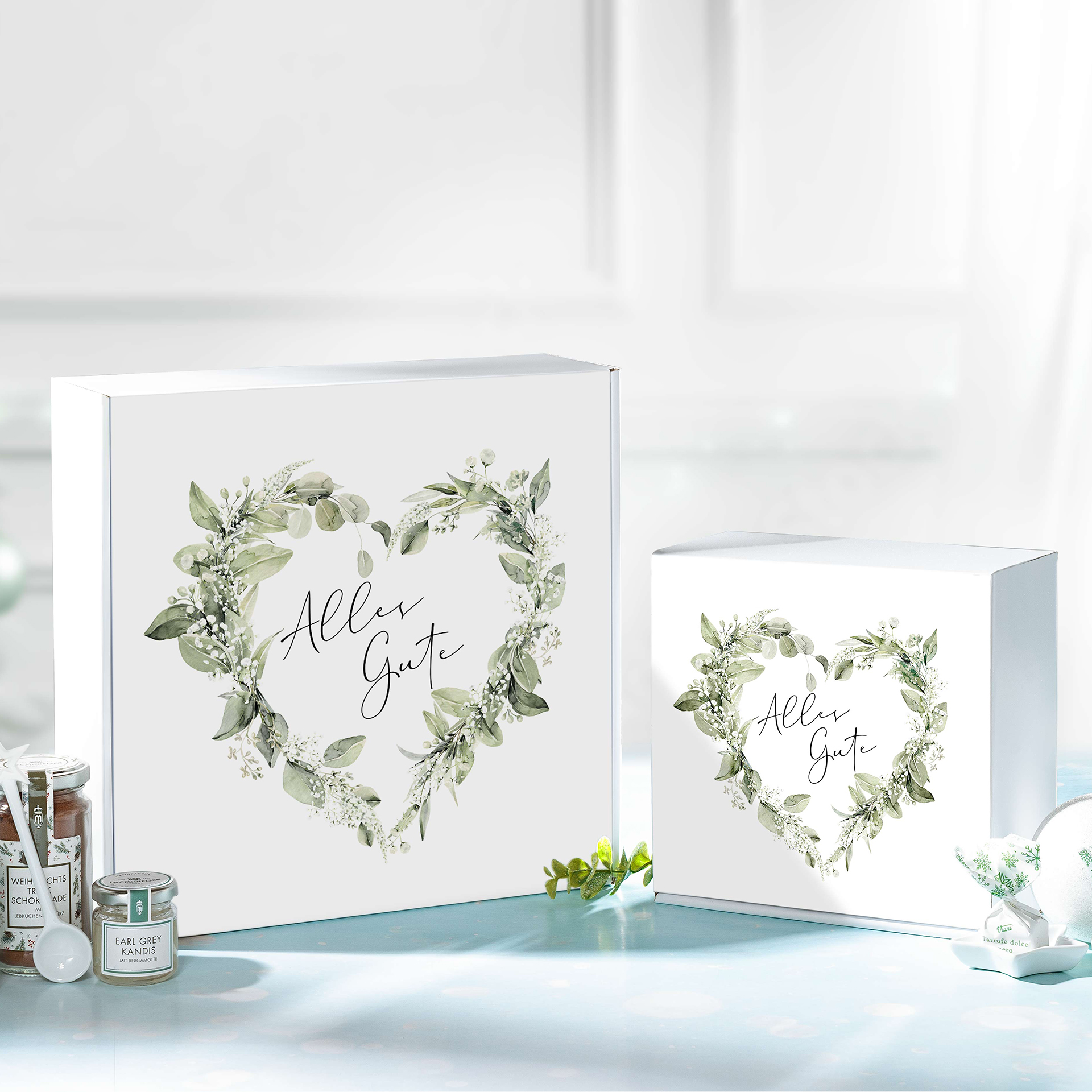 Weiße Geschenkboxen mit grünem Blattkranz und "Alles Gute"-Schriftzug im Quadrat